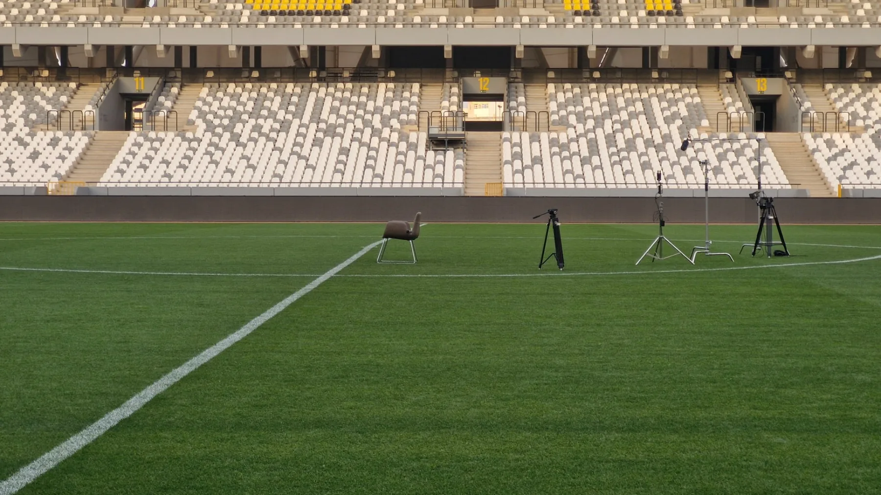 A single chair, tripod and light stand alone on a stadium pitch before the shoot begins