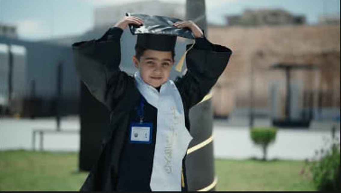 A child in a graduation gown lifting his cap