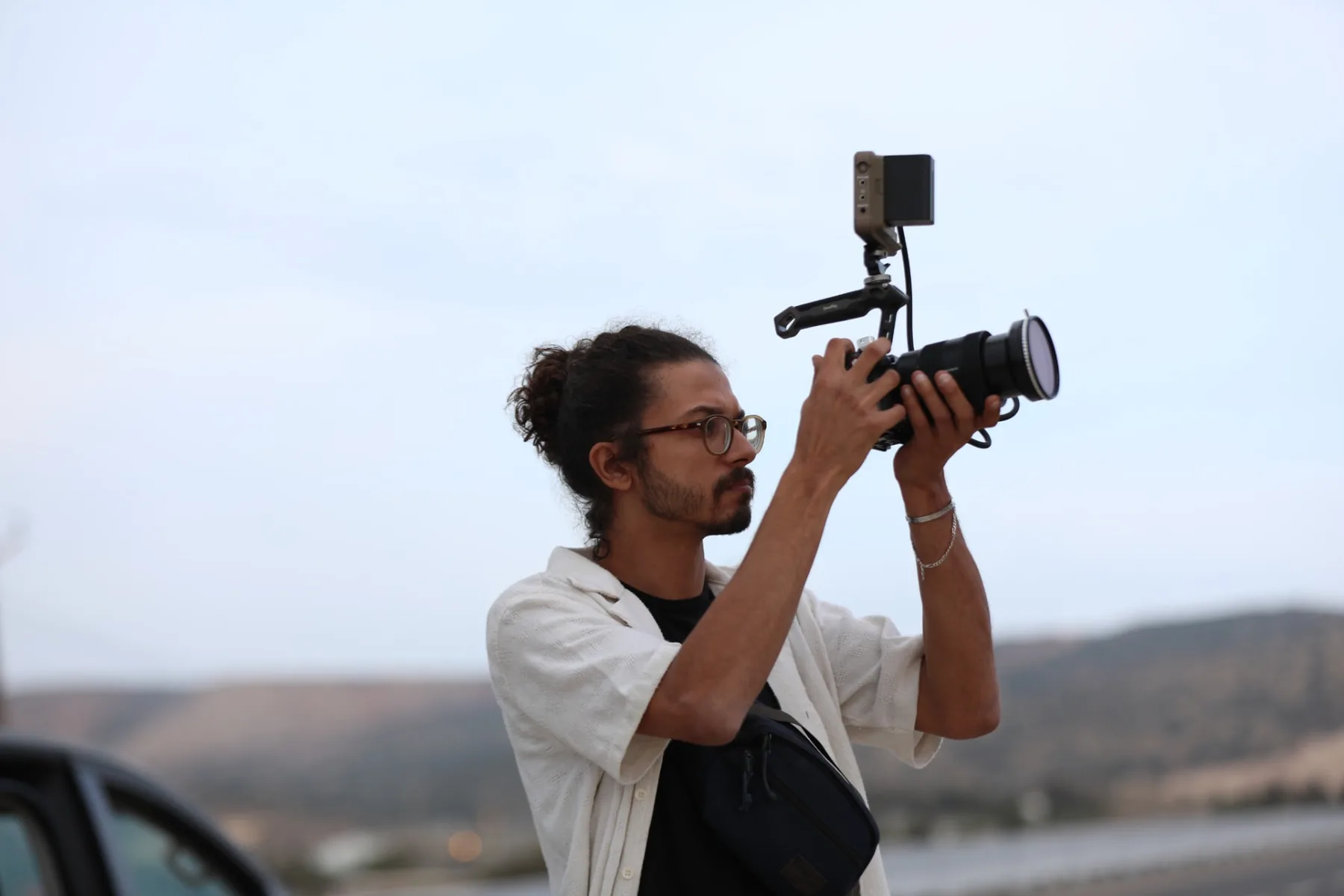 Asaad raising a shoulder-rigged cinema camera to frame a shot on an open road at dusk