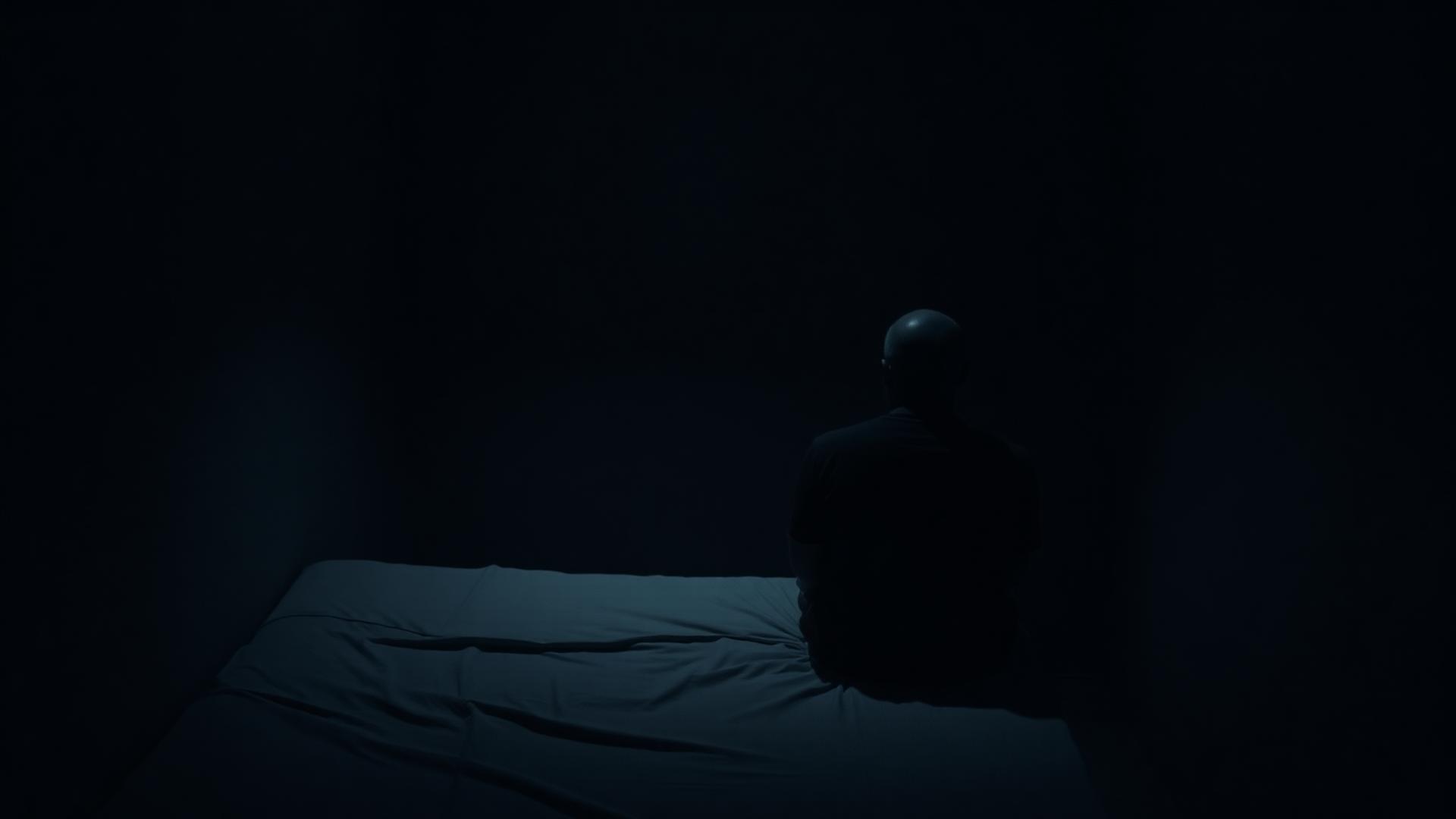 A man alone at the edge of a bed at dawn